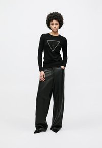 Μαύρο πουλόβερ με μακριά μανίκια, με τριγωνική λεπτομέρεια λογότυπου και ερωτηματικό, συνδυασμένο με μαύρο, φαρδύ παντελόνι από συνθετικό δέρμα.