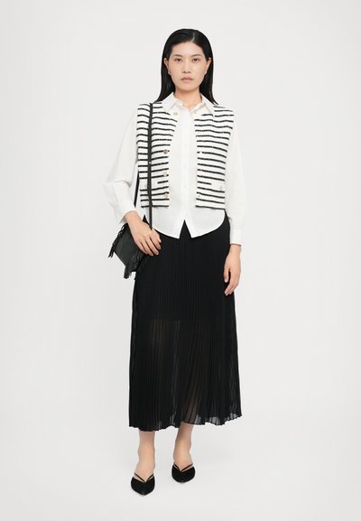 Vit blus med svarta ränder, plisserad svart kjol och svart handväska. Outfiten inkluderar spetsiga svarta skor och en ren design.
