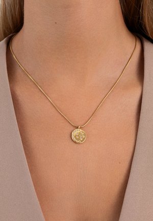 Collana d'oro con un ciondolo circolare liscio, decorato con piccole gemme disposte in un motivo decorativo, su una catena sottile e texturizzata.