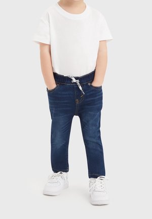 Denim-Jogginghosen mit elastischem Bund, dunkelblau, mit Fronttaschen, kombiniert mit einem weißen T-Shirt und weißen Sneakers.