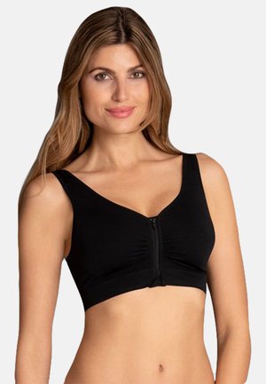 Woman with long hair wearing a black front-zip sports bra, smiling, against a plain light background.