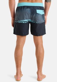 Shorts de bain pour hommes en noir avec un effet ombragé et des accents en teal. Comprend une poche à l'arrière et un marquage latéral. Le matériau semble léger.