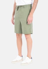 Shorts verde oliva realizzati in tessuto leggero, con vita elasticizzata e due tasche laterali. Abbinati a sneakers bianche.