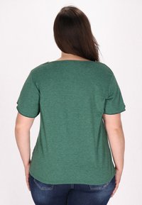 Cămașă verde cu mânecă scurtă, realizată dintr-un material moale, texturat. Are un decolteu bateau și mâneci răsucite, cu accesorii decorative pe umăr.