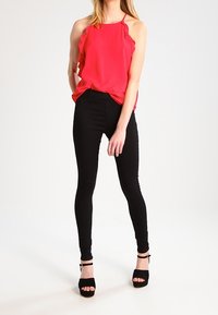 Top sin mangas rojo con acentos de volantes, combinado con pantalones ajustados negros y sandalias de tacón alto negras. Tejido suave con un corte relajado.