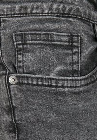 Tissu en denim noir avec un tissage en sergé texturé, comportant une poche arrière et un accent en rivet en métal argenté. Détails de décoloration subtile visibles.