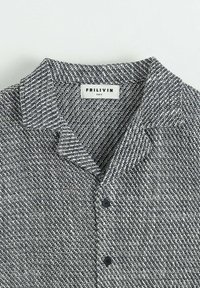 Chemise tissée noir et blanc avec col, fermeture par boutons et tissu texturé. L'étiquette indique "FRILIVIN, taille S."