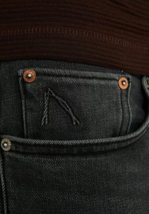 Donkerdenim jeans met een voorzak met een gestikt ontwerp, koperen hardwareaccenten en een gestructureerde afwerking.