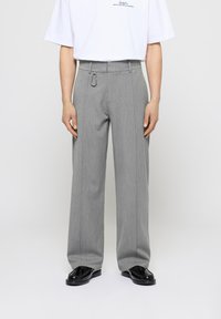 Pantalones de pierna ancha gris, hechos de una tela texturizada, con un lazo para cinturón con un acento metálico, combinados con una camisa blanca de manga corta.
