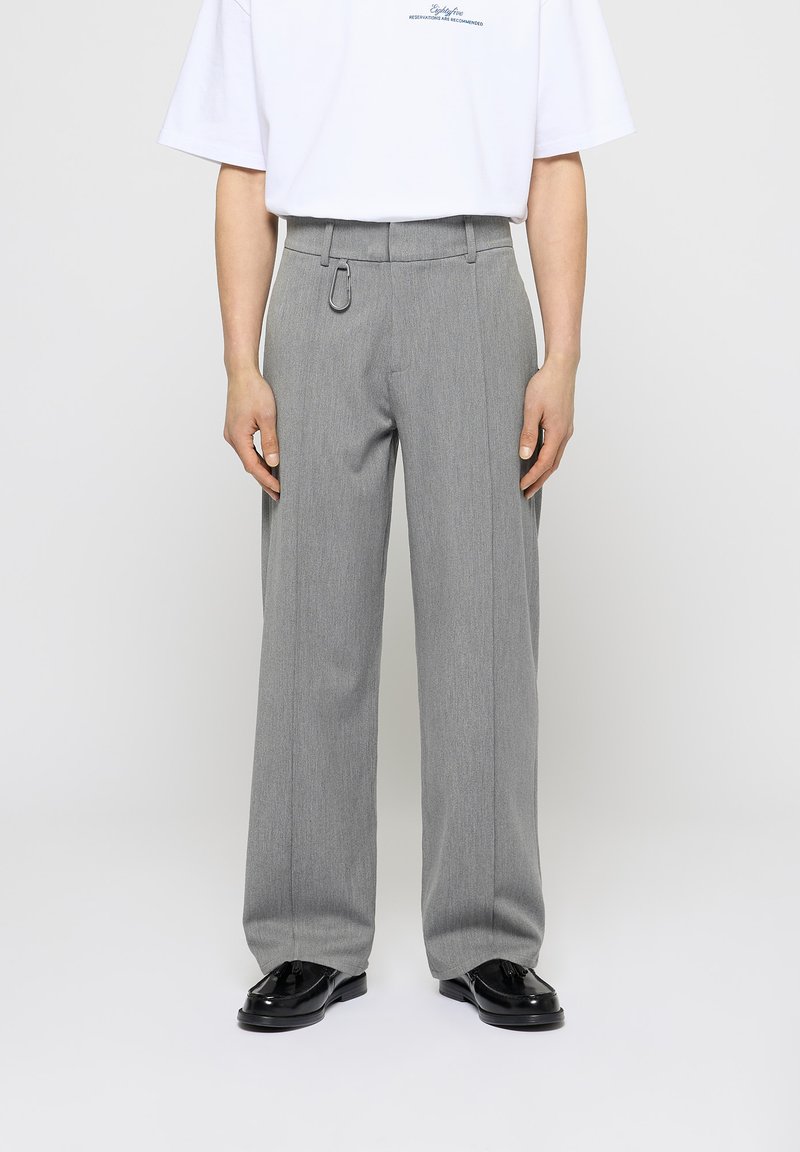 Pantalones de pierna ancha gris, hechos de una tela texturizada, con un lazo para cinturón con un acento metálico, combinados con una camisa blanca de manga corta.