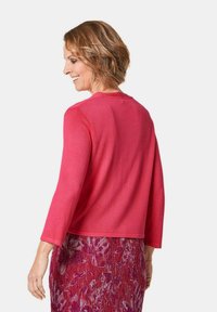 Roze, lichtgewicht trui met driekwartmouwen, ronde hals en een gladde tekstuur. Draagt over een gebloemde, knie-lange rok.