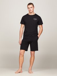 Zwart katoenen t-shirt met wit logo op de linker borst, gecombineerd met zwarte shorts. De pasvorm is relaxed en de stof lijkt glad en lichtgewicht.