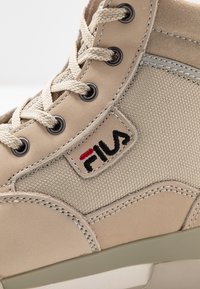 Sneaker alto beige realizzato in una combinazione di pelle liscia e tessuto testurizzato, con cuciture grigie e un logo rosso e nero.