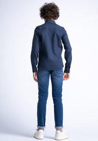 Camicia button-up blu in misto cotone con una texture liscia. Abbinata a jeans slim-fit blu e sneakers bianchi.