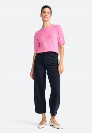 Pull en maille fuchsia à manches courtes associé à un jean en denim foncé taille haute et des ballerines blanches à bout pointu. Design simple et épuré avec une coupe décontractée.