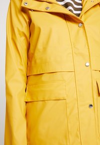 Veste de pluie jaune imperméable avec fermeture zippée à l'avant, boutons-pression et deux poches avant. Texture lisse avec une coupe décontractée.