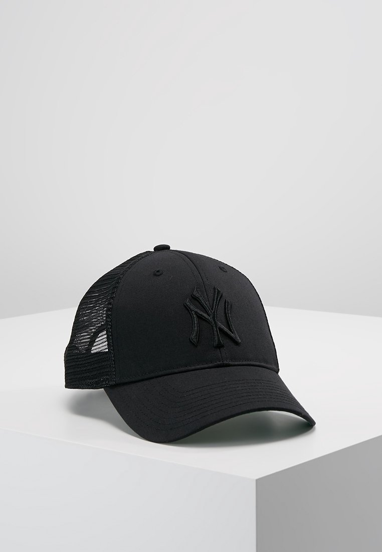 Casquette de baseball noire en mesh avec visière incurvée et logo en relief à l’avant, posée sur une surface blanche sur fond gris uni.