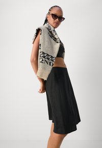 Strikket sweater i beige med sorte mønstre, stylet over en sort cropped top og en sort, knælang A-line nederdel. Cat-eye solbriller fuldender looket.