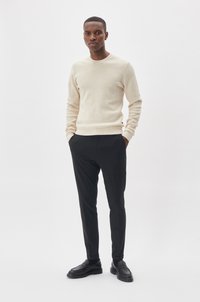 Lichtbeige gebreide trui met lange mouwen, gecombineerd met zwarte slim-fit broeken en zwarte instappers. Eenvoudig, aansluitend ontwerp.