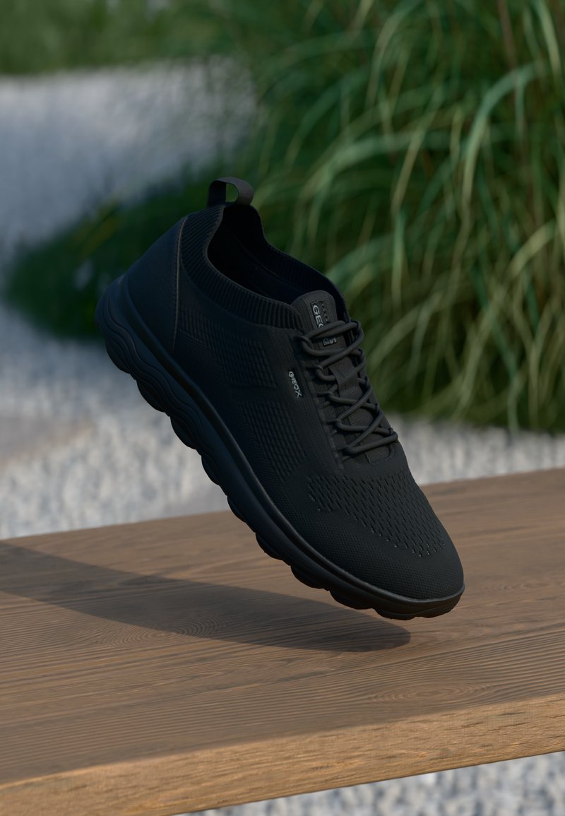 Black athletic shoe with a breathable mesh upper, textured design, lace-up front, and cushioned sole, displayed on a wooden surface.