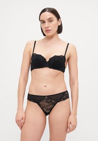 Zwart kanten lingerie set bestaande uit een balconette beha met geschulpte randen en een bijpassende doorzichtige slip met bloemenpatroon. Zachte textuur, minimale hardware.