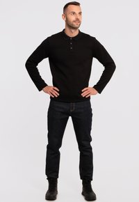 Svart långärmad polo med krage och tre knappar, i kombination med mörkblå jeans och svarta snörkängor.