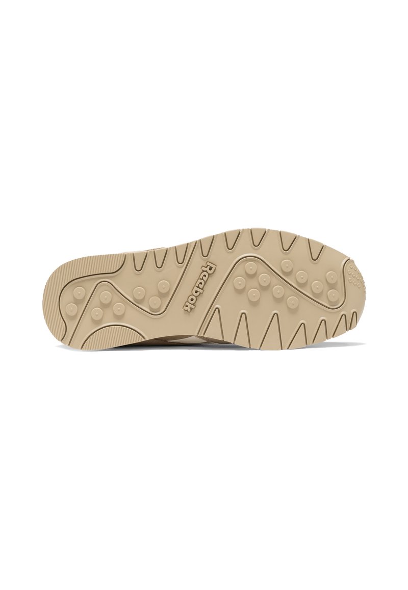 Semelle de sneaker beige clair avec un motif texturé en vagues et des grips circulaires. Marquage Reebok au niveau de la partie médiane.