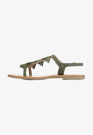 Sandali piatti verde oliva con dettagli in frange. Design con punta aperta, suola piatta e cinturino alla caviglia regolabile. Texture liscia, stile minimalista.