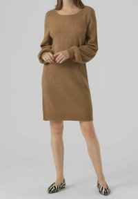 Robe pull en tricot marron à coupe droite, décolleté rond et manches bouffantes. Des ballerines à rayures zèbre noires et blanches complètent le look.