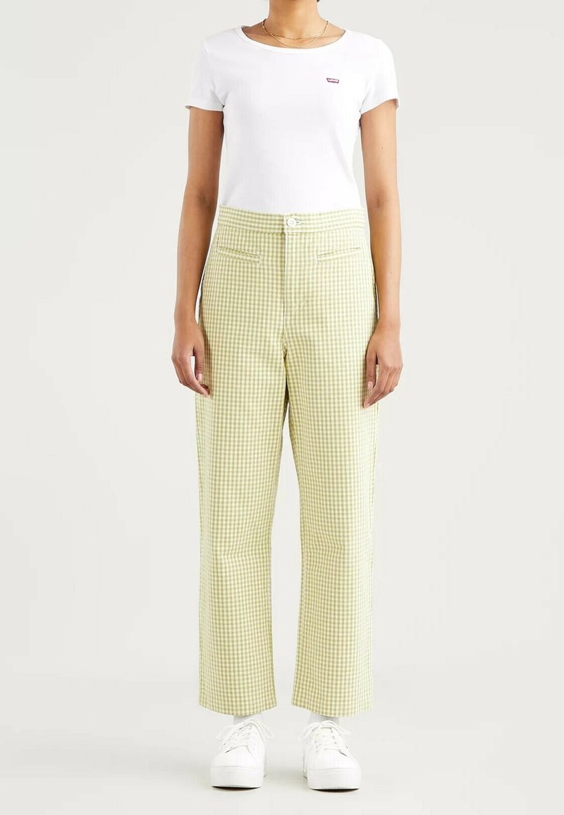 Pantalon à carreaux verts et blancs avec une taille haute, des jambes droites, deux poches avant et une fermeture à boutons, associé à un t-shirt blanc.