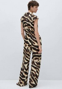 Jumpsuit s uzorkom životinja, kratki rukavi, smešano smeđa i bež boja, ležeran kroj i široke nogavice. Glatka tkanina s sjajnom završnom obradom.