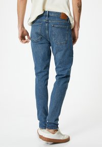 Jeans in denim blu con una vestibilità tapered, dotati di cinque tasche, patch in pelle sul retro e una leggera scoloritura per un aspetto testurizzato.
