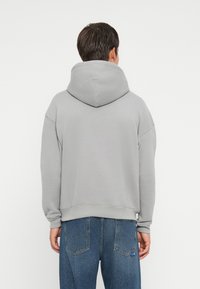Grå hættebluse med en løs pasform, der har en stor hætte og ribbede manchetter, parret med blå jeans. Enkel og uden udsmykninger.