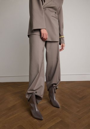 Costume beige ajusté avec un pantalon large et une veste à double boutonnage. Bottines à talons brillantes en cuir reptile avec des bouts pointus.