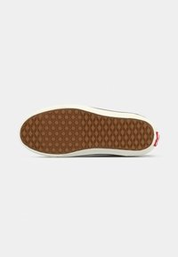 Rubber sole of a black shoe with diamond and hexagonal tread pattern, white midsole, and small red branded tag at heel.