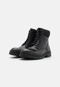 Botas de cuero negras con un cuello de tela gris texturizada, punta redonda, cierre con cordones y suela de goma negra rugosa.