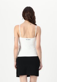 Hvit ribbestrikket tanktopp med tynne stropper, med logo-tekst på baksiden, kombinert med et svart a-linje mini skjørt. Glatt tekstur.