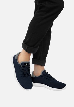 Granatowe siatkowe sneakersy z szarymi akcentami. Biała gumowa podeszwa, okrągły czubek i płaskie sznurowadła. Noszone z podwiniętymi czarnymi spodniami.
