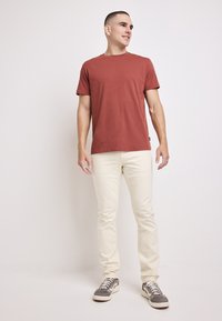 Czerwono-rdzawa bawełniana koszulka z okrągłym dekoltem, krótkie rękawy, zestawiona z beżowymi dżinsami slim-fit i szarymi trampkami z białymi akcentami.