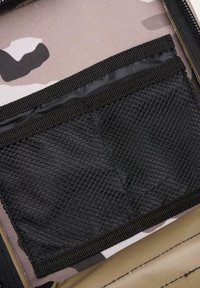 Kamuflažni shranjevalni etui z bež in svetlo rožnato zasnovo, ki vključuje črn mrežast žep in rebrast rob. Vidna teksturirana tkanina.