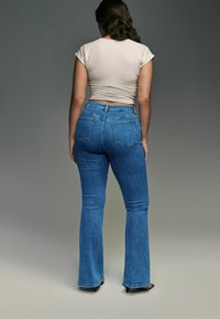 Blauwe uitlopende jeans met een middelhoge taille en een vijf-pocket ontwerp, gecombineerd met een fitted beige cropped t-shirt, gezien vanuit de achterkant.