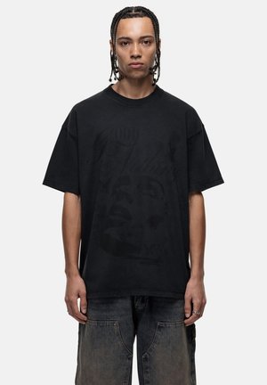 Zwarte oversized t-shirt met een verouderde afwerking. Voorzien van een vervaagde afbeelding van een gezicht en tekst op de voorkant. Korte mouwen en ronde hals.