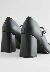 Scarpe nere con tacco alto in finitura in pelle liscia, con tacchi quadri e una sottile cinghia alla caviglia, che mostrano un design elegante.