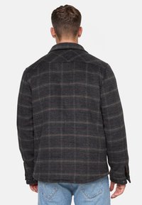 Wzorzysta wełniana kurtka w ciemnoszarym i czarnym kolorze z czerwonymi akcentami, z wyraźnym kołnierzem, zapinanymi mankietami i prostym dołem.