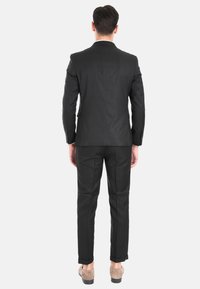 Giacca e pantaloni neri visti da dietro. Vestibilità su misura, tessuto morbido, rever stretto e spalle strutturate. Scarpe eleganti visibili.