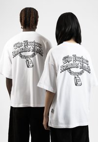 Camisetas blancas de gran tamaño con un gráfico negro en la parte trasera, que representa una cadena y un candado con el texto "El horizonte sigue oscuro."