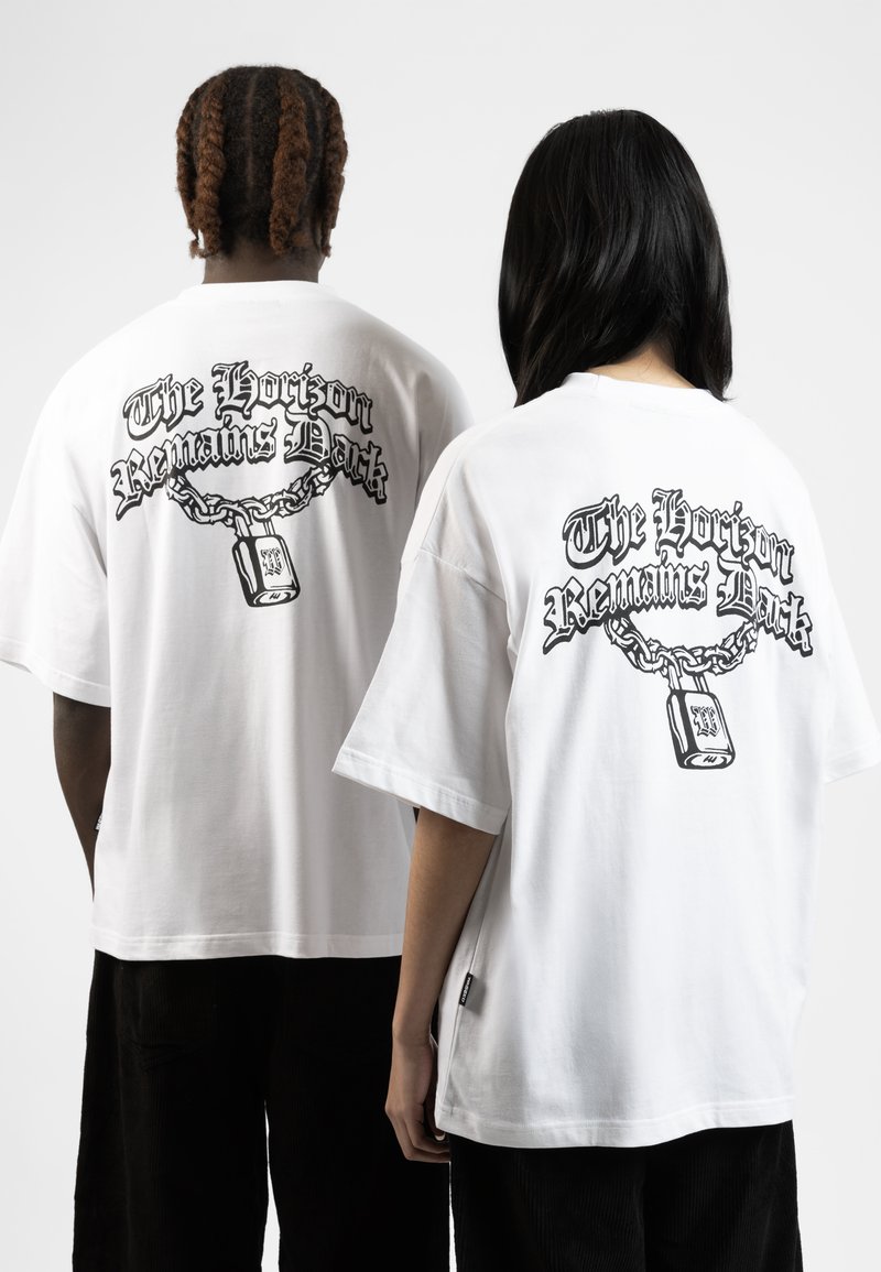 Camisetas blancas de gran tamaño con un gráfico negro en la parte trasera, que representa una cadena y un candado con el texto "El horizonte sigue oscuro."