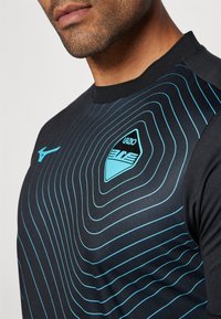 Camiseta deportiva negra con diseño de patrones de olas azules, cuello redondo y un logo que presenta la palabra "Lazio" y un emblema en la zona del pecho.
