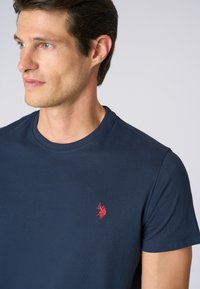 T-shirt in cotone blu navy con scollatura rotonda e maniche corte. Presenta un piccolo logo ricamato rosso nella parte sinistra del petto.