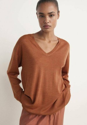 Pull V en couleur rouille avec des manches longues, une coupe décontractée et une texture douce. Le tissu tombe confortablement et présente des poches latérales.